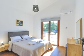 Un dormitorio con cama, mesita de noche y un ventanal con vistas al verdor.