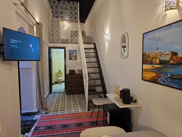 Ein Hotelzimmer mit Treppe, einem Fernseher, der eine Google TV-Oberfläche anzeigt, einem Gemälde einer Küstenansicht und einem gemusterten Teppich.