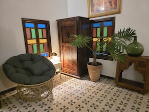 Une pièce avec un fauteuil en rotin, une plante en pot, un meuble en bois et un sol carrelé.