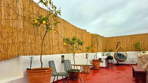 An outdoor seating area with wicker chairs, a hanging chair, and potted plants against a bamboo wall. - Riad Boutique Baba (Rabat)