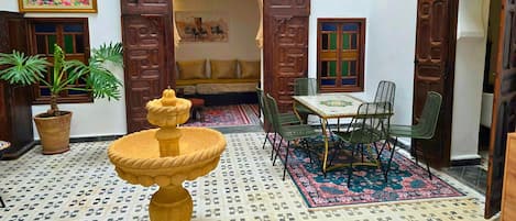 A traditional Moroccan interior with a fountain, a dining area, and a sofa set.