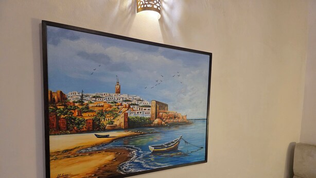 A painting of a coastal town with buildings, a beach, and boats on the water. - Riad Boutique Baba (Rabat)