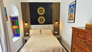 A bedroom with a bed, a dresser, a nightstand, a wall with a decorative pattern, and a window with colored glass panes. - Riad Boutique Baba (Rabat)