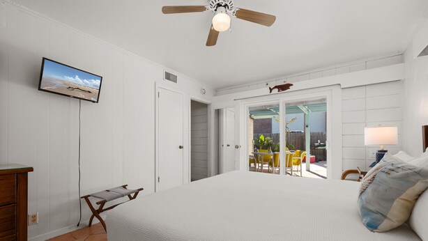 Ein Schlafzimmer mit einem Bett, einem Deckenventilator, einem an der Wand befestigten Fernseher und Blick auf die Außenpatio.
