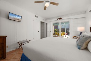 A bedroom with a bed, a ceiling fan, a TV on the wall, and a view of the outside patio. - Poolside Oasis | Walk to the Beach (South Padre Island)