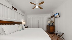 Ein Schlafzimmer mit Bett, Deckenventilator, Kommode, Fernseher und Spiegel.