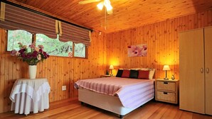 Een kamer met houten lambrisering, een bed, bedlampen, een nachtkastje en een raam met jaloezieën.