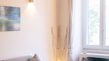 Una sala moderna con un sofá, una mesita de centro y una silla. Se ve una ventana con cortinas, un cuadro en la pared y una lámpara.