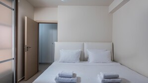 A modern hotel room with a large bed, white linens, and two folded towels on the bed. - Omega House in Crete (Ligaria)
