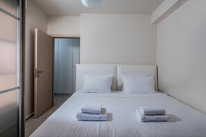 Ein modernes Hotelzimmer mit einem großen Bett, weißen Bettwäsche und zwei gefalteten Handtüchern auf dem Bett.