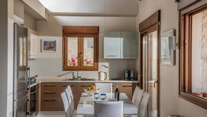 A modern kitchen with wooden cabinets, a dining table with chairs, and a window with a view of the outside. - Omega House in Crete (Ligaria)