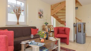 A cozy living room with a brown sofa, red armchairs, a coffee table with magazines and a wine bottle, a fireplace, and a staircase. - "Rotmilan," a thatched-roof vacation home with a sauna and fireplace in a quiet location on Rügen (Neuenkirchen)