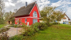 A red house with a thatched roof, surrounded by a garden and trees. - "Rotmilan," a thatched-roof vacation home with a sauna and fireplace in a quiet location on Rügen (Neuenkirchen)