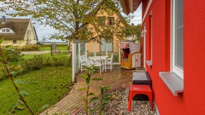 Eine Terrasse mit Tisch und Stühlen, eine kleine Holzkonstruktion und eine rote Wand.