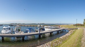 Ein Yachthafen mit mehreren Booten an den Liegeplätzen, eine Holzsteganlage und eine Wiese am Wasser.