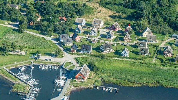 An aerial view of a lakeside village with houses, a marina, and boats. - "Rotmilan," a thatched-roof vacation home with a sauna and fireplace in a quiet location on Rügen (Neuenkirchen)