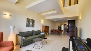 A spacious living area with a sofa, coffee table, and a piano. - George's Poet Maisonette (Rethymno)