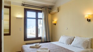 A hotel room with a bed, two wall-mounted lights, a window with curtains, and an air conditioning unit. - George's Poet Maisonette (Rethymno)