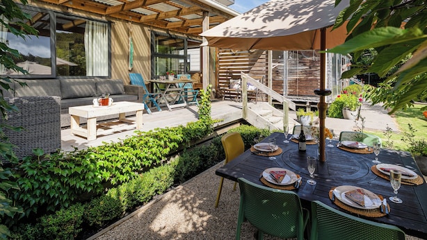 En uteplats med ett träbord dukat för måltider, en soffa och en överbyggd sittplats med en pergola ovanför.