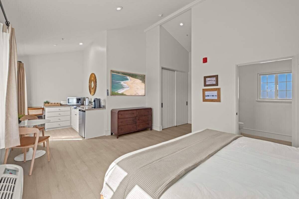 A bedroom with a bed, a desk, a dresser, and a painting of a beach.