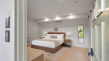 A bedroom with a bed, bedside tables, a mirror, and a view of greenery outside.