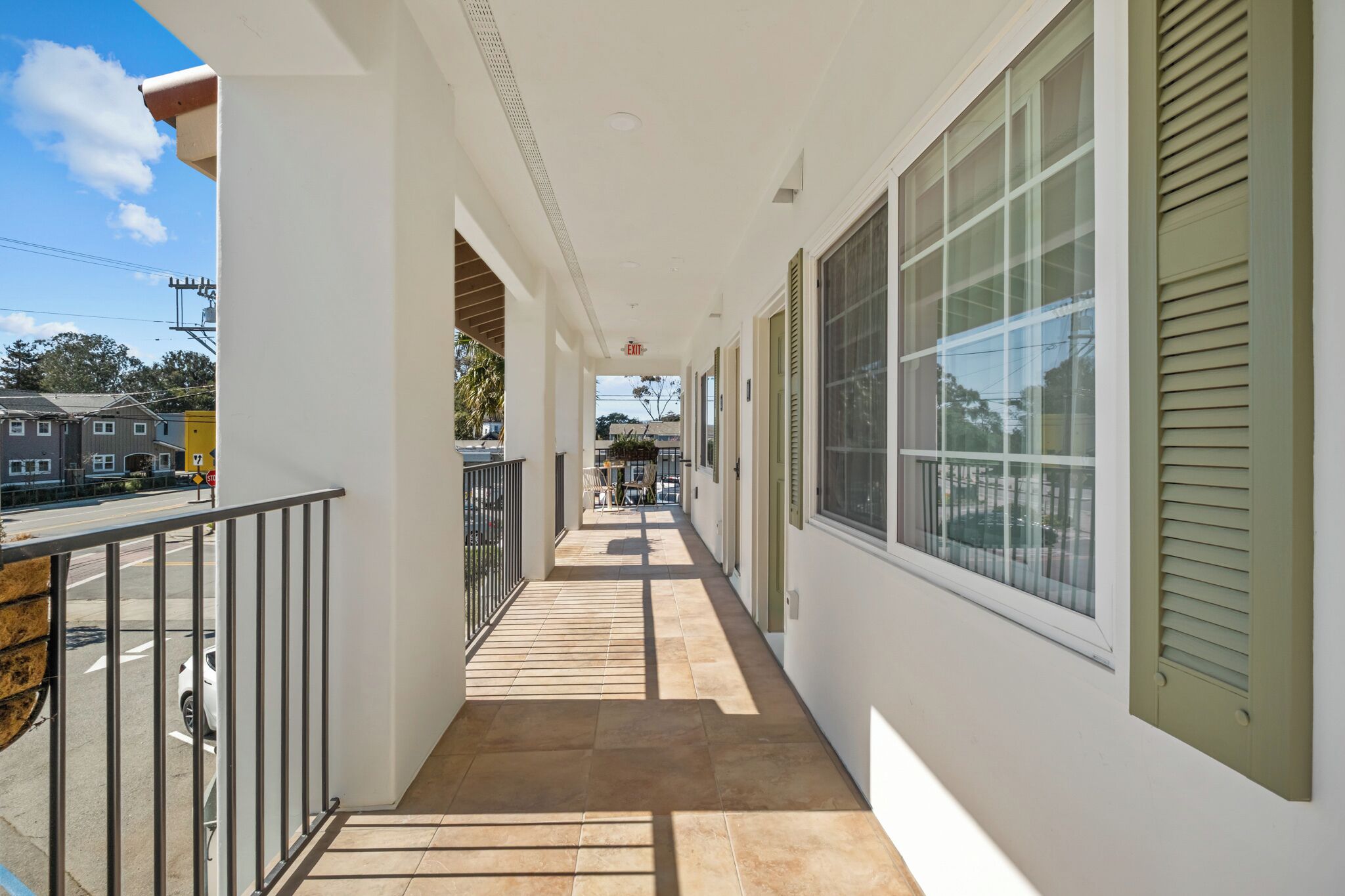 A corridor with a balcony, large windows, and a view of the street.