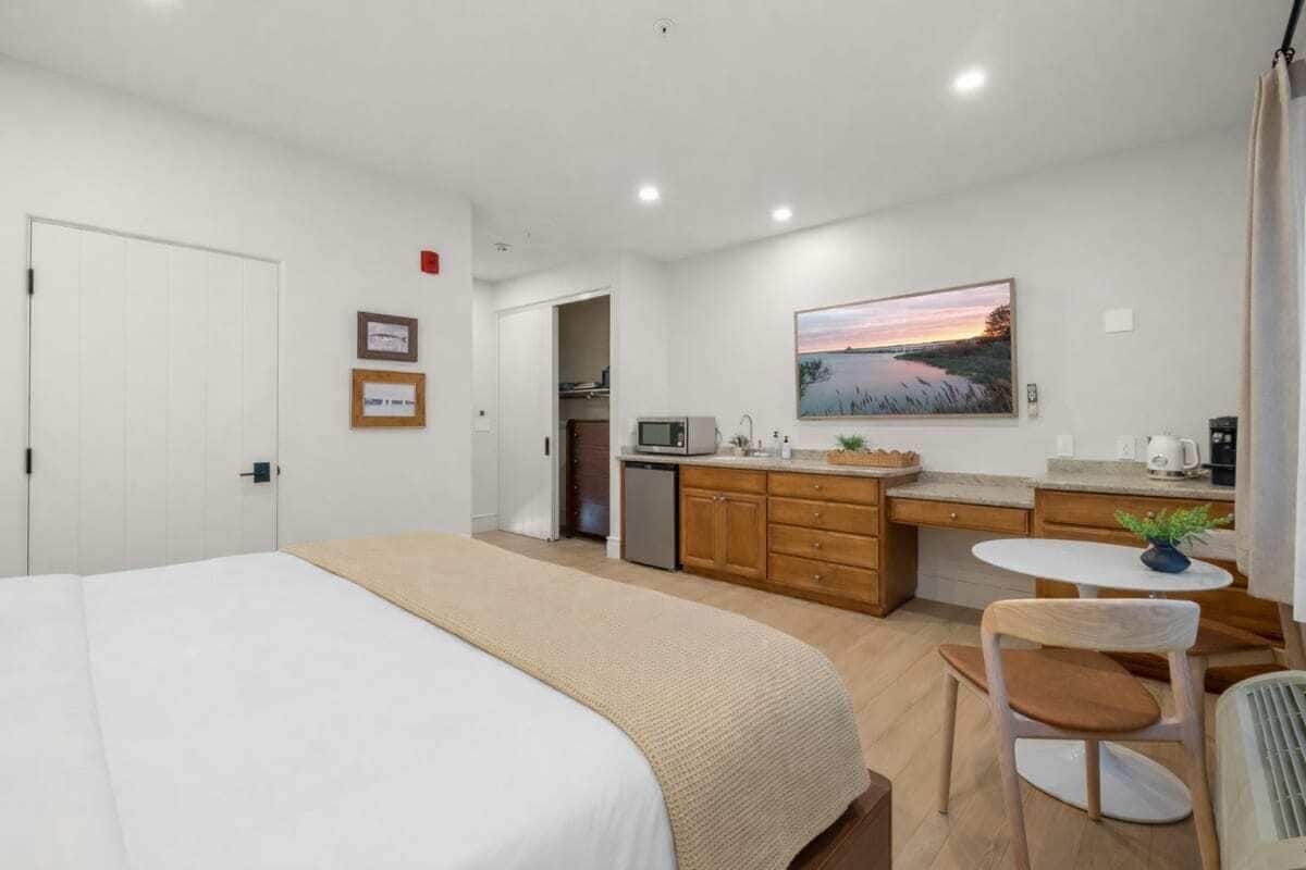 A hotel room with a bed, a kitchenette, a dining area, and a painting on the wall.