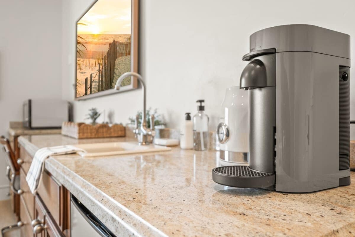 Une cuisine équipée d’une machine à café, d’un évier et d’un miroir qui reflète le coucher de soleil.
