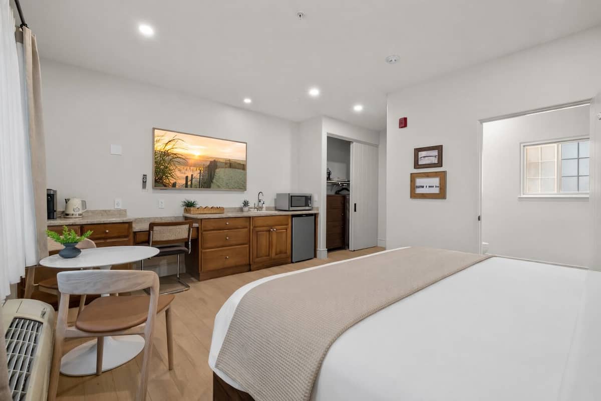 A hotel room with a bed, a small kitchenette, a dining area, and a bathroom.