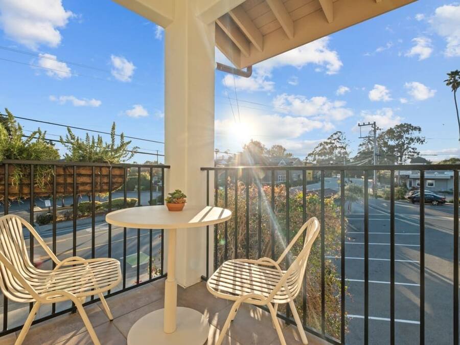 A balcony with two chairs and a table, overlooking a street with cars and trees.