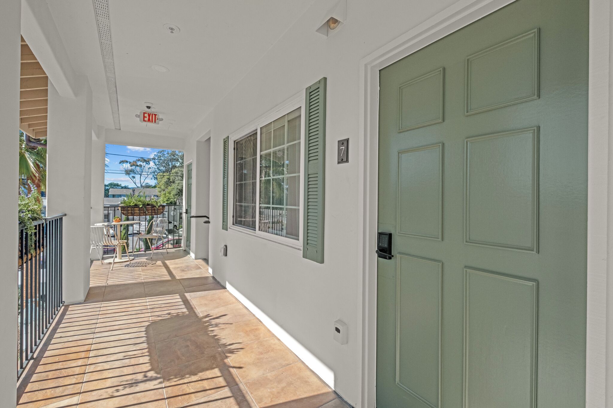 A corridor with a green door, a window with shutters, and a view of the outside.