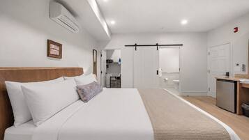 A modern hotel room with a large bed, a bedside table, a wardrobe, a bathroom, and a kitchenette.