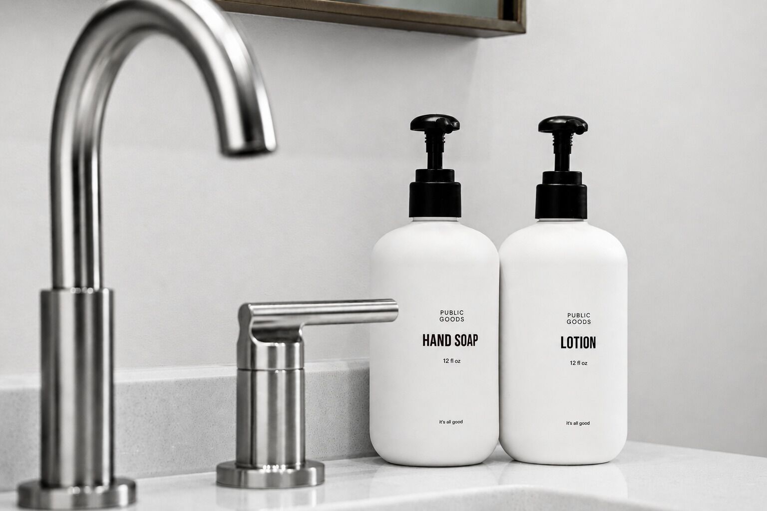A bathroom with a modern faucet, two bottles of hand soap and lotion, and a mirror above the sink.