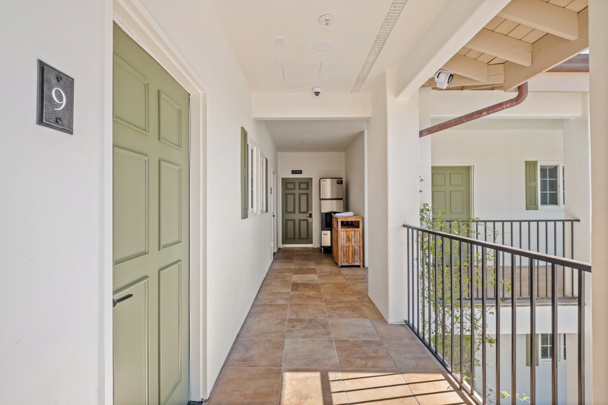 A hallway with a green door, a refrigerator, and a small wooden cabinet.
