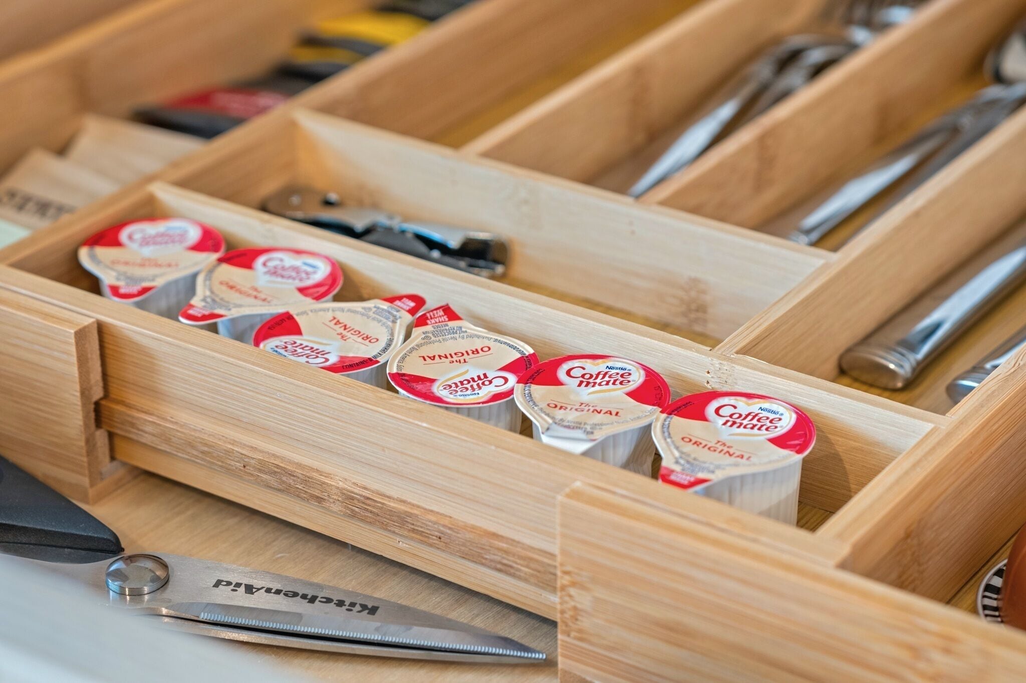 A wooden drawer containing coffee creamer tubes and a pair of scissors.