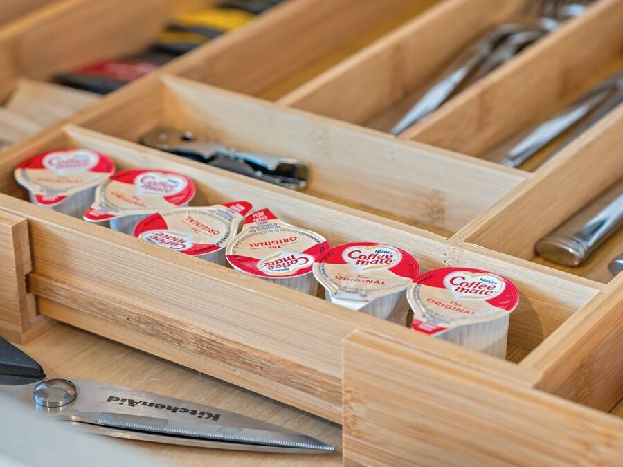 A wooden drawer containing coffee creamer tubes and a pair of scissors.