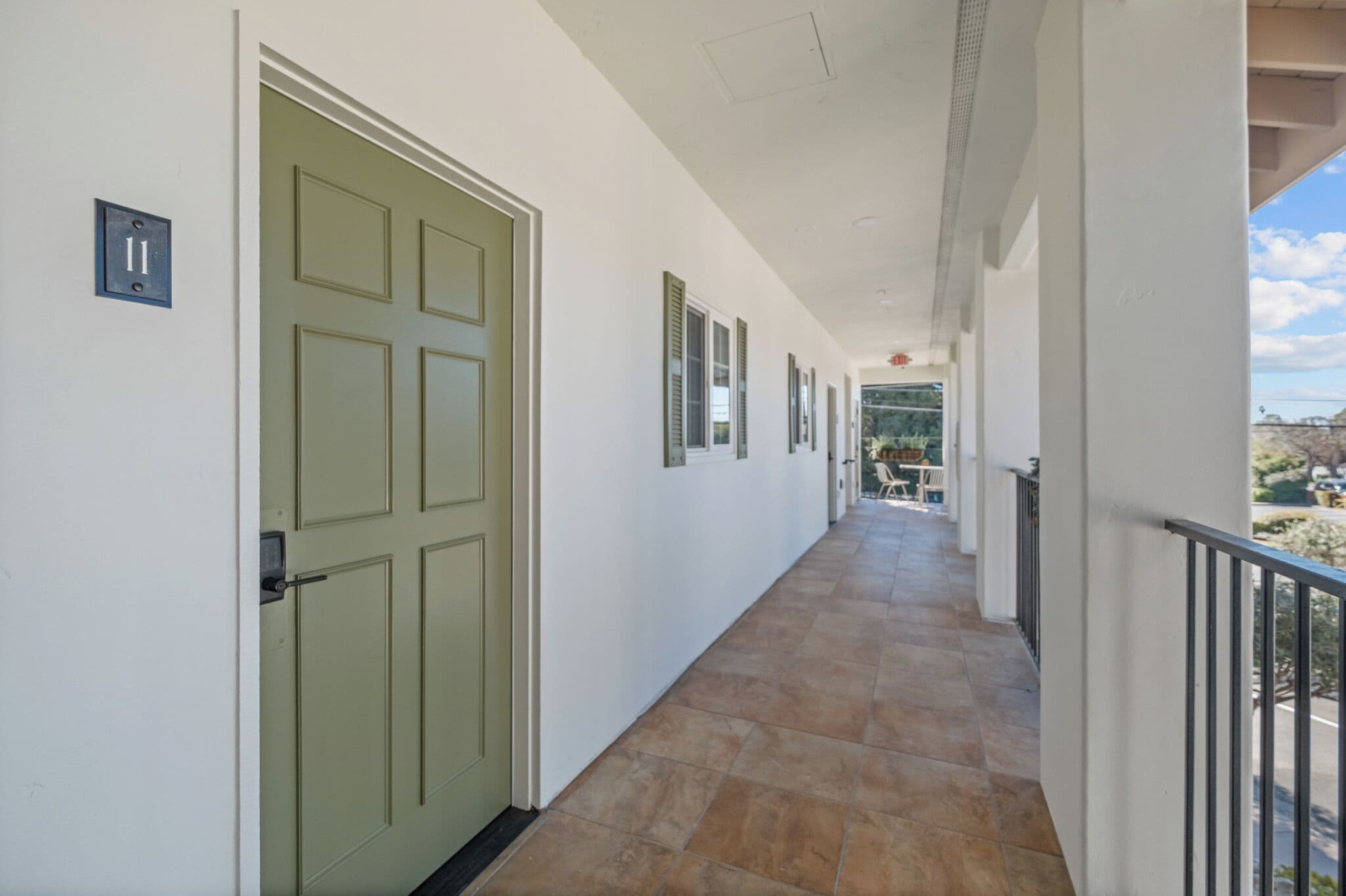 A corridor with a green door, a light switch, and a view of the outside.