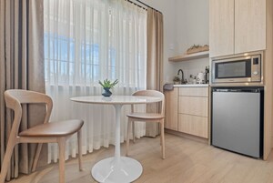 A modern kitchen with a microwave, refrigerator, and wooden cabinets. There is a round dining table with two chairs and a potted plant.