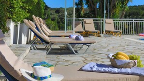 Un espace aménagé au bord de la piscine, avec des chaises longues, des parasols et un panier de fruits.