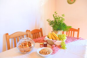 A dining table with a bowl of cookies, a bowl of grapes, a basket of bananas, and a potted plant. - Alexandra Bay Front in Άγιος Στέφανος (Agios Stefanos)