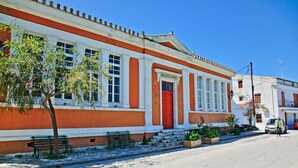 Ein Gebäude mit roter Tür und weißen Säulen, einer Bank und einem Baum davor.