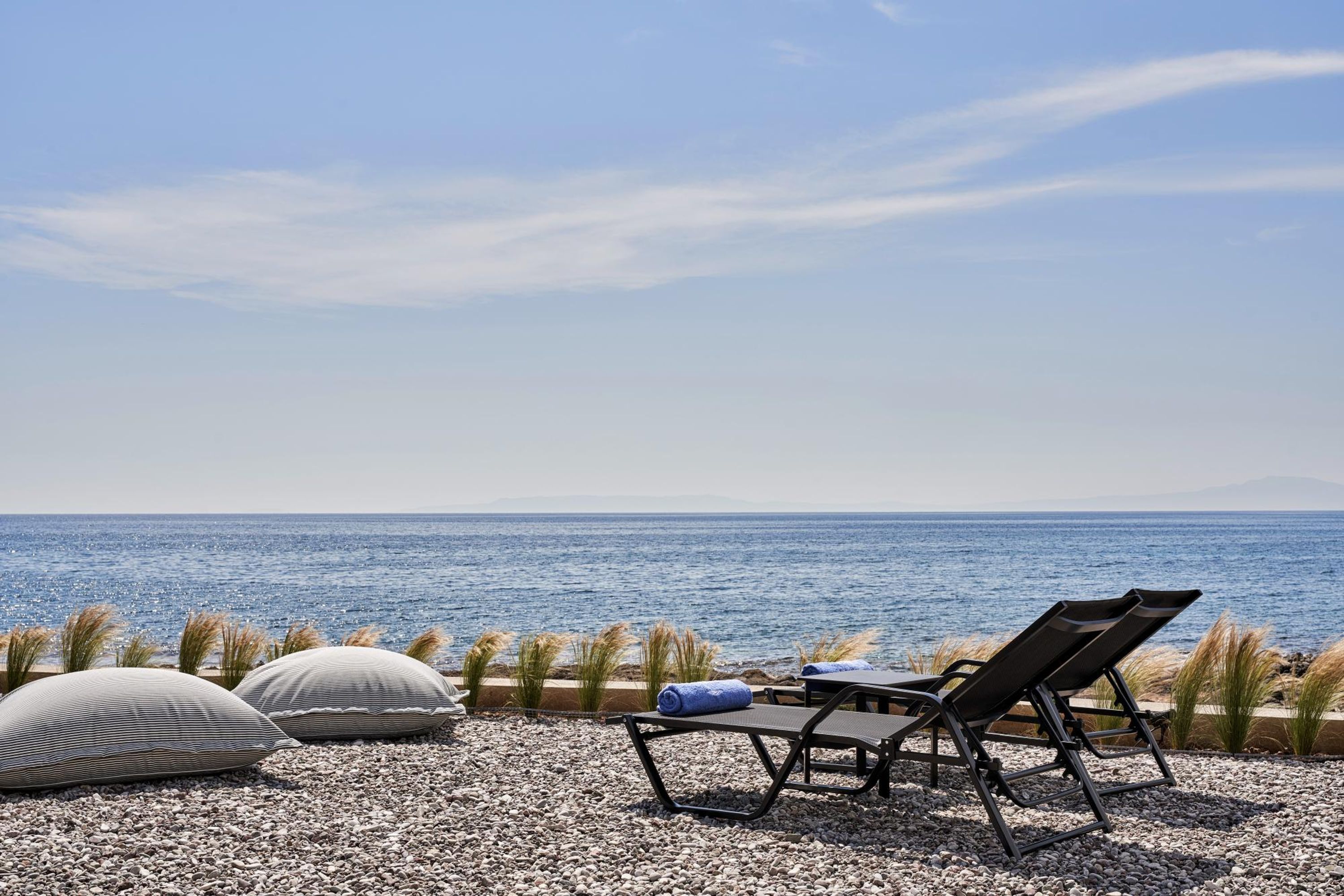 Zona relax in spiaggia con vista sul mare, comprende una poltrona prendisole, un tavolino e cuscini decorativi.