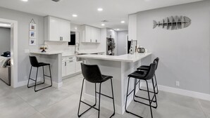 Une cuisine moderne avec des meubles blancs, un îlot central doté de tabourets de bar et un tableau décoratif représentant des poissons.