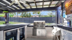 Une cuisine extérieure équipée d’un barbecue à gaz, de placards intégrés et d’un ventilateur de plafond.