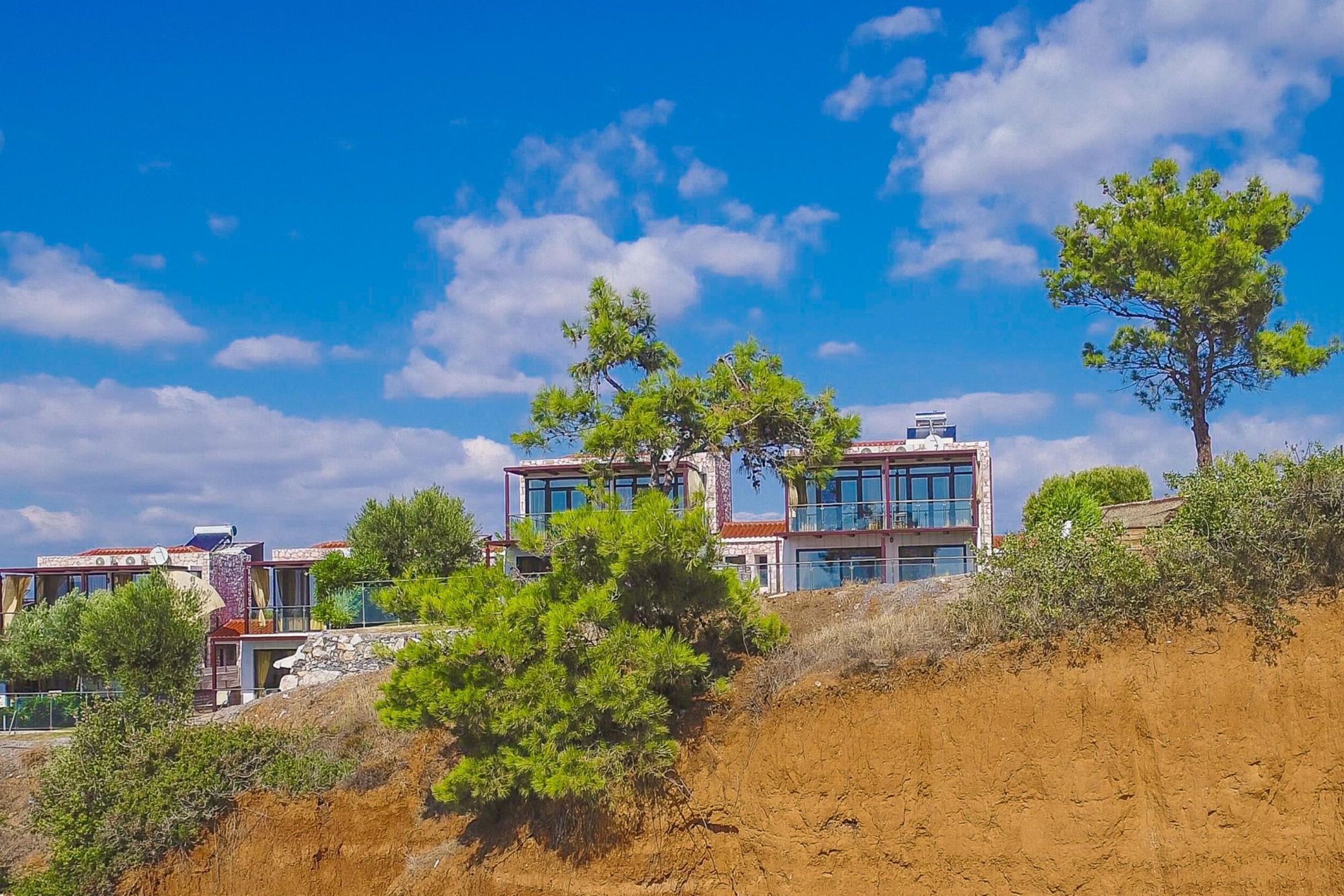 Un bâtiment moderne à deux étages, doté de grandes fenêtres et d’un toit plat, entouré d’arbres et situé dans un paysage vallonné.