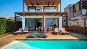 Uma casa moderna de dois andares com piscina, área de estar externa e vista para o mar.