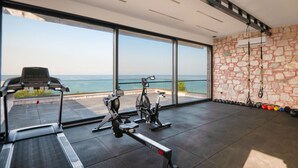 Academia com aparelhos de cardio, pesos e vista para o mar.