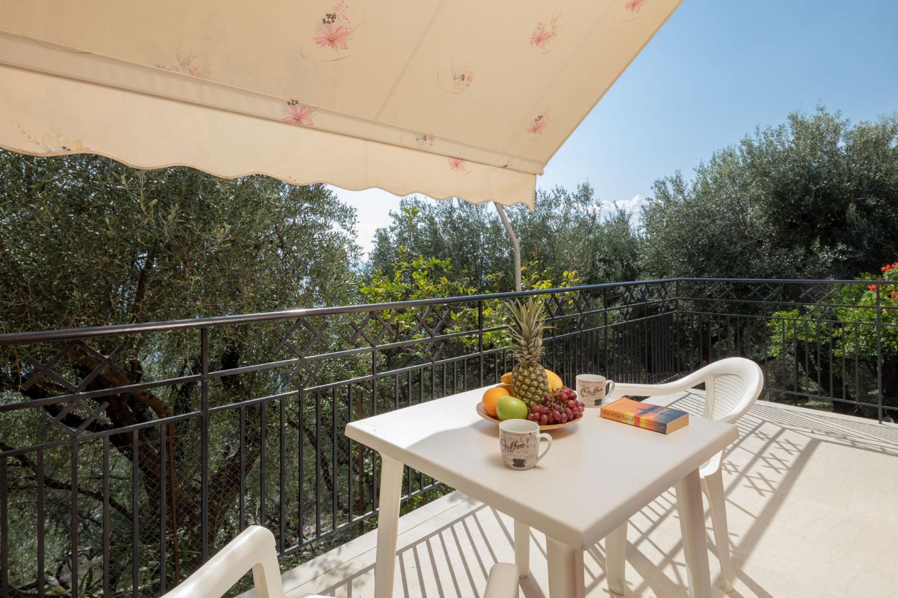 A balcony with a table, chairs, a fruit bowl, a pineapple, a book, and a coffee mug.