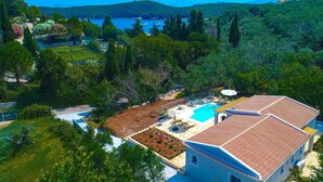A house with a swimming pool, tennis court, and lush greenery surrounding the property. - Villa Jupeter in Corfu (Corfu)