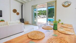A modern living room with a large wooden table, white sofa, and a glass door leading to a pool area. - Villa Jupeter in Corfu (Corfu)